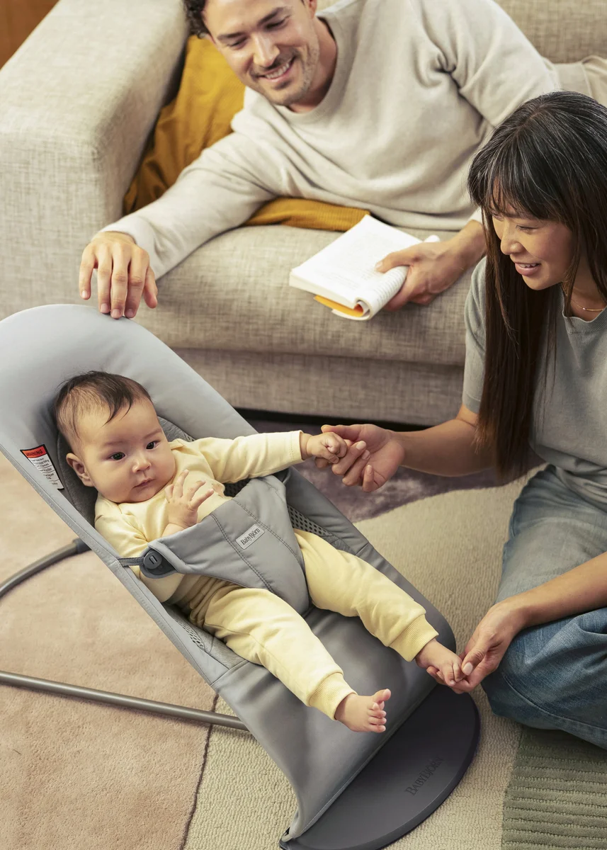 Parents sitting with their baby in a BabyBjörn Bouncer Balance Soft in a living room