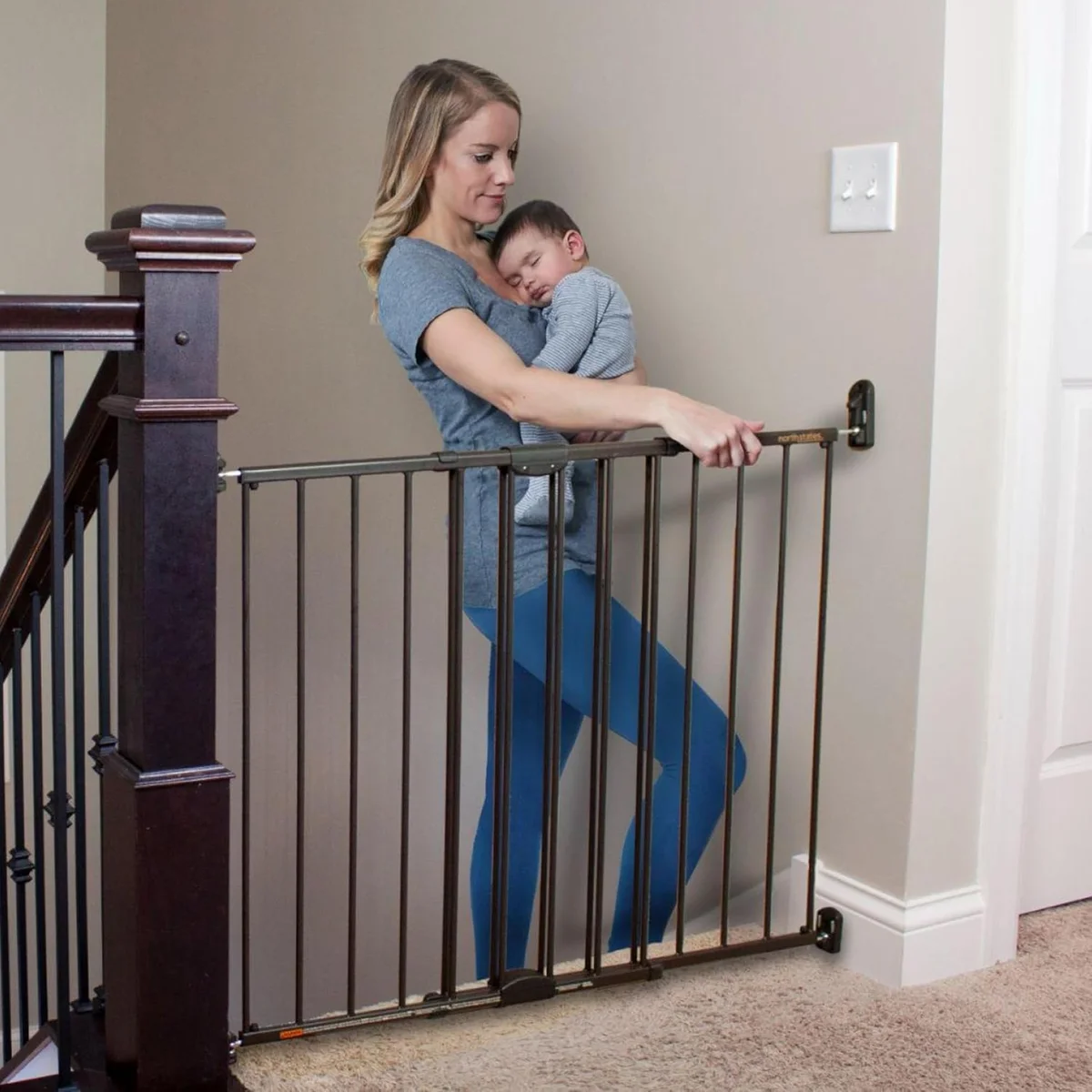 Parent holding toddler stepping through the open Toddleroo Easy Swing & Lock gate at a staircase landing