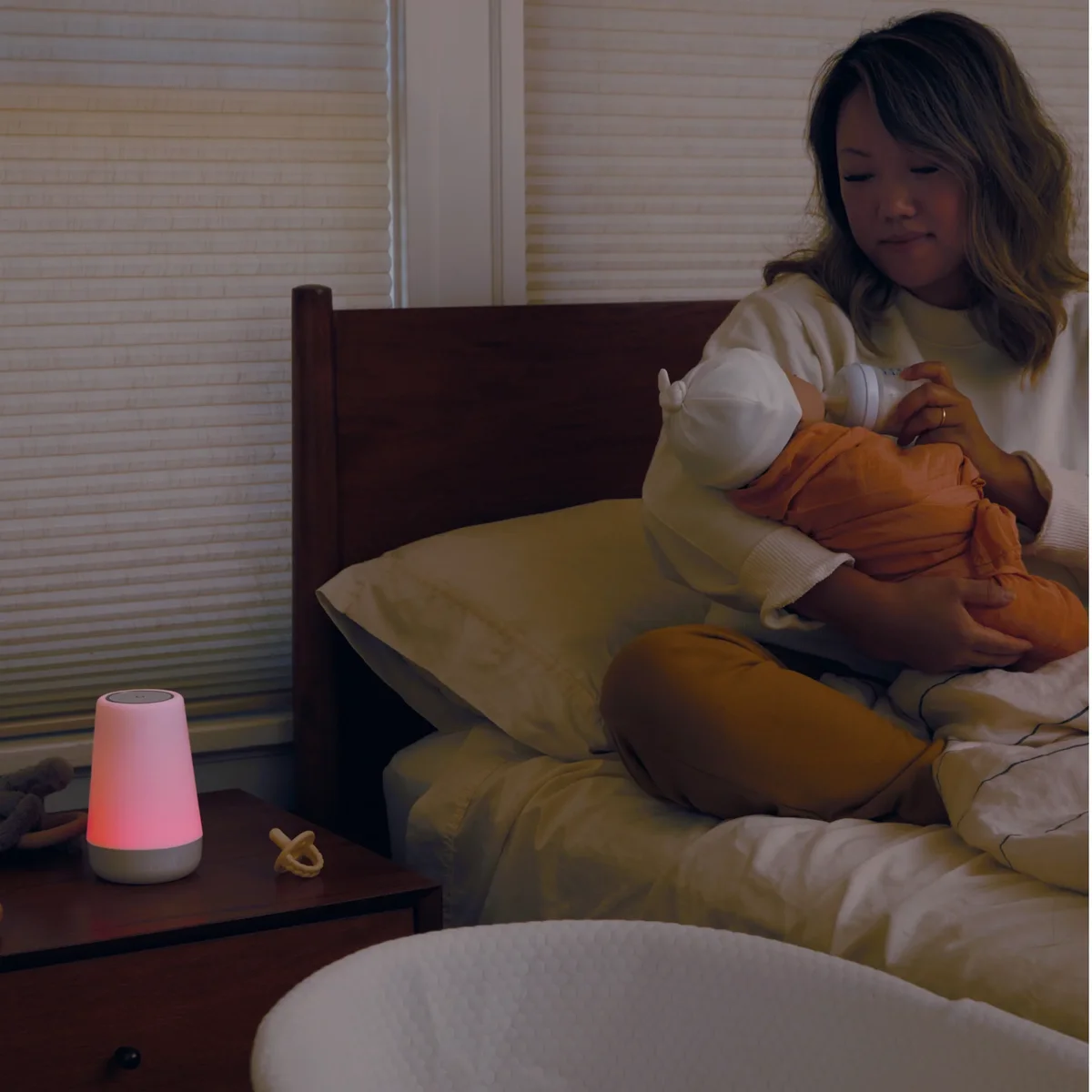 Hatch Rest 2nd Gen glowing red on bedside table while mother feeds newborn