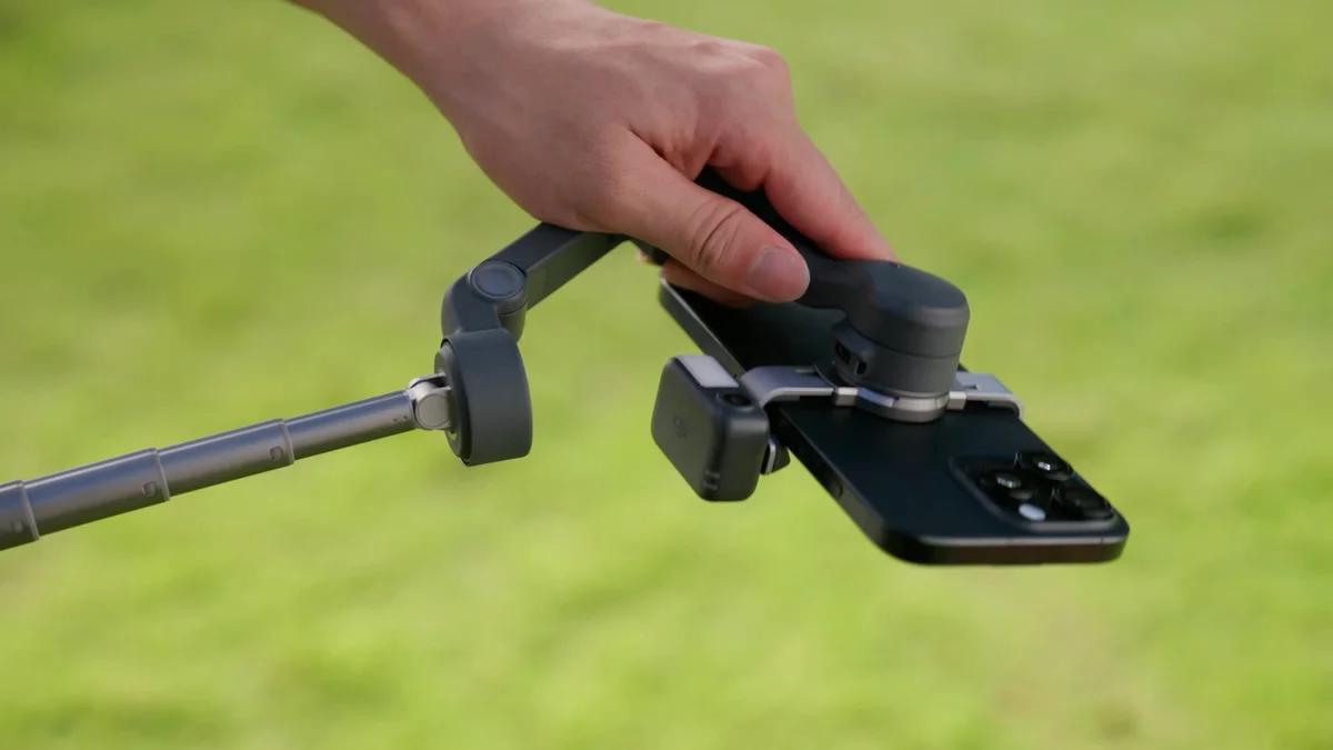 DJI Osmo Mobile 8 held by hand outdoors with tripod legs extended and phone attached