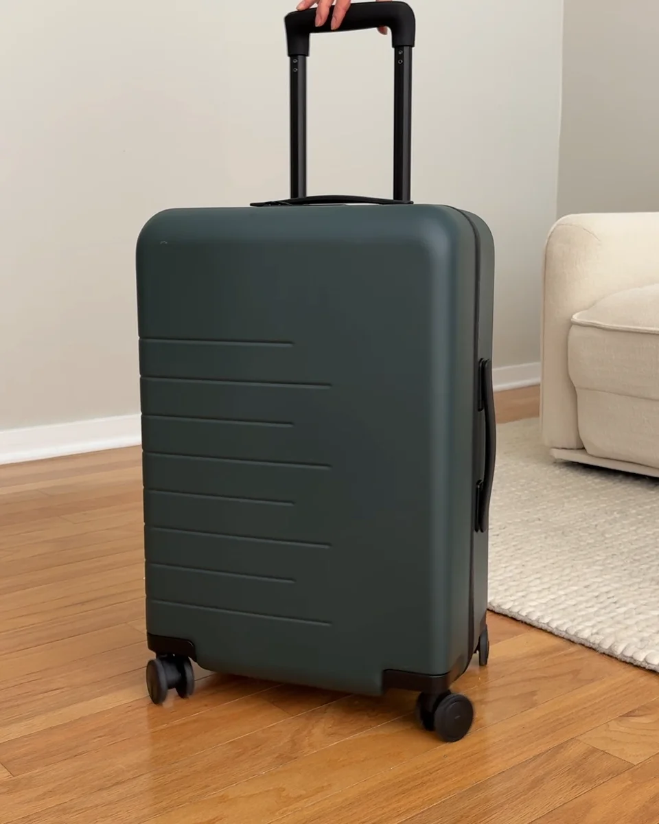 Quince Carry-On Hard Shell Suitcase in dark green with telescoping handle extended, lifestyle shot