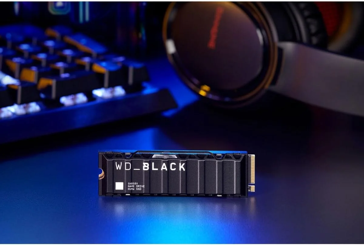 WD_Black SN850X heatsink SSD on a gaming desk beside a mechanical keyboard and headset under blue lighting