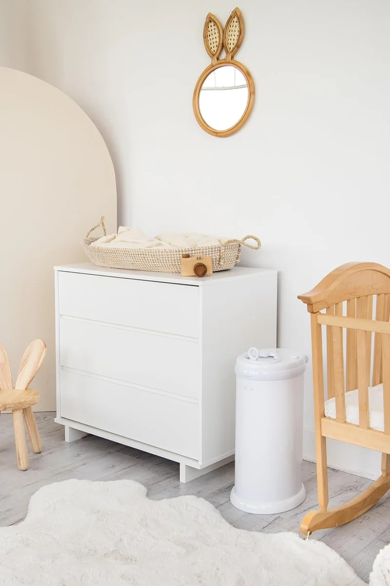 Ubbi Steel Diaper Pail in white styled in a modern Scandinavian nursery beside a wooden crib
