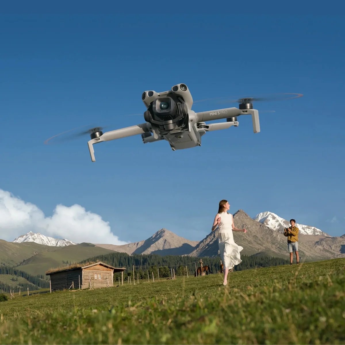 DJI Mini 5 Pro in flight over alpine meadow with operator in background