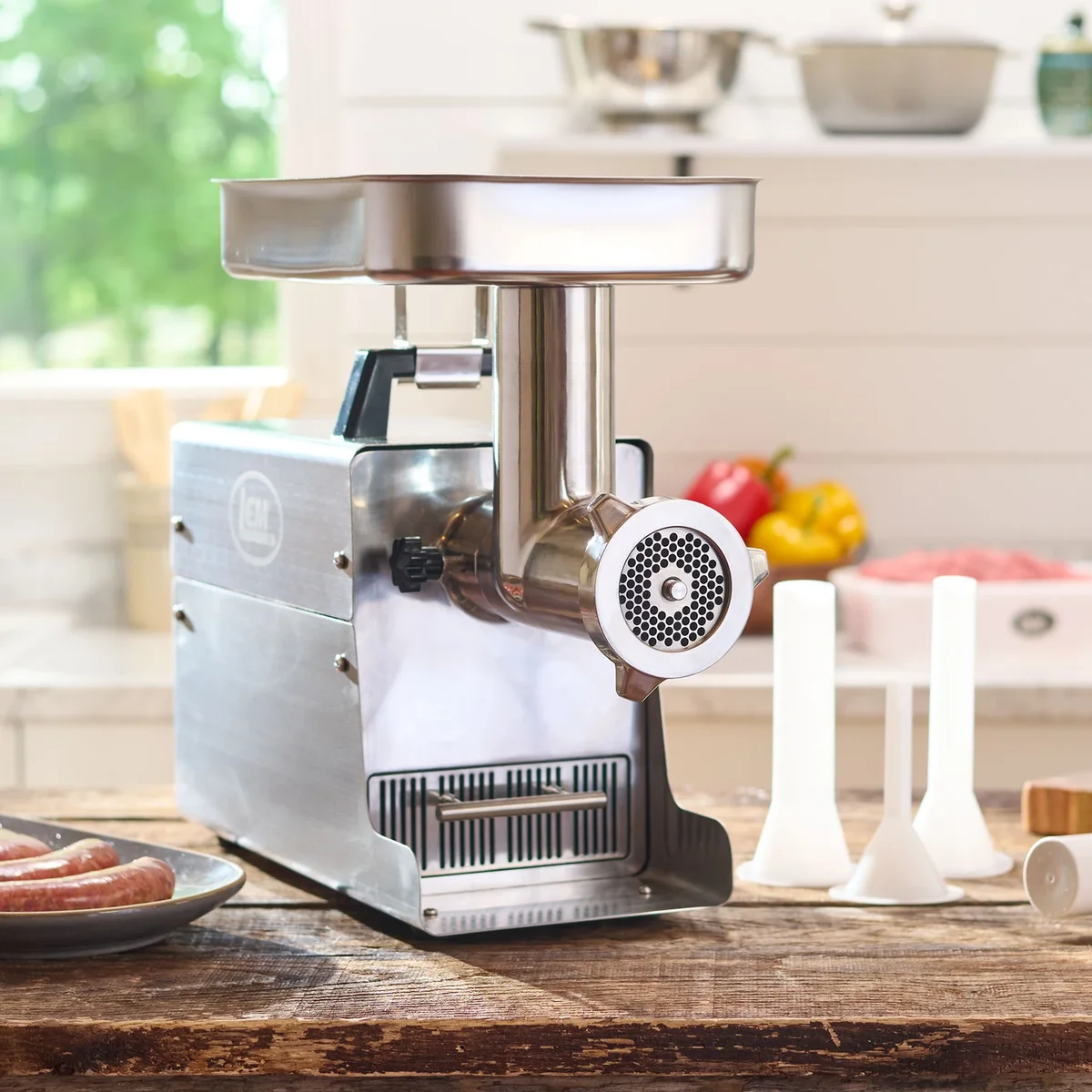 LEM Big Bite #8 meat grinder in use on a wooden kitchen counter beside fresh sausages, peppers, and stuffing tubes