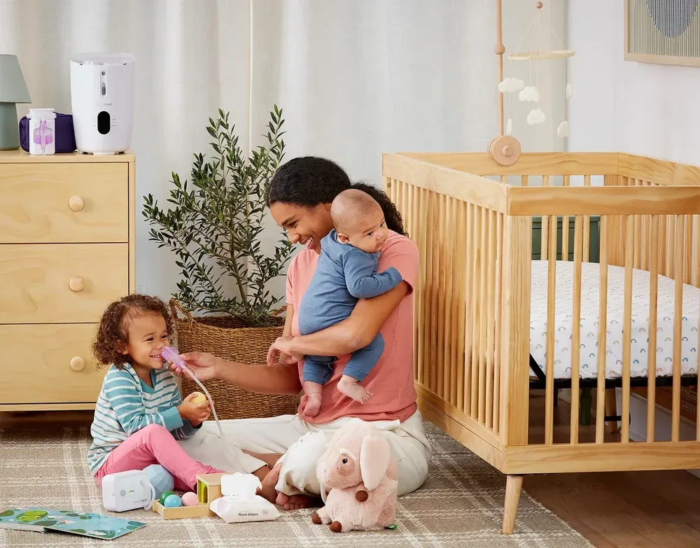 Parent using the Dr. Noze Best NozeBot with a toddler in a nursery beside the crib