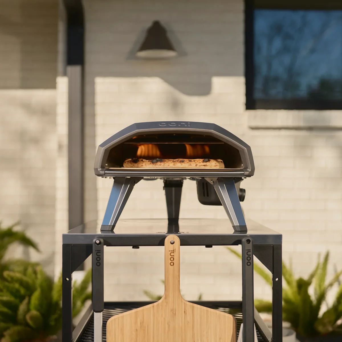 Ooni Koda 2 outdoors with a Neapolitan pizza cooking on the stone and flames visible through the oven mouth