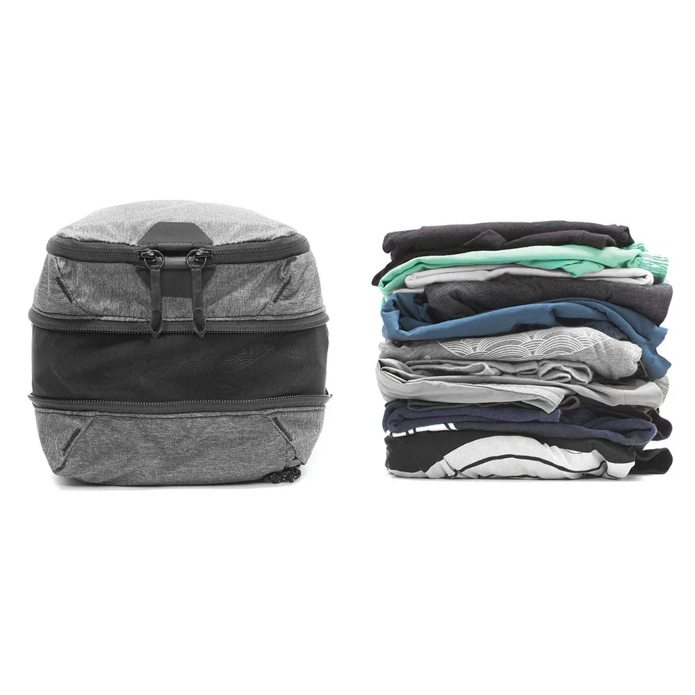Peak Design Packing Cube open and expanded next to a large stack of folded clothes, showing capacity