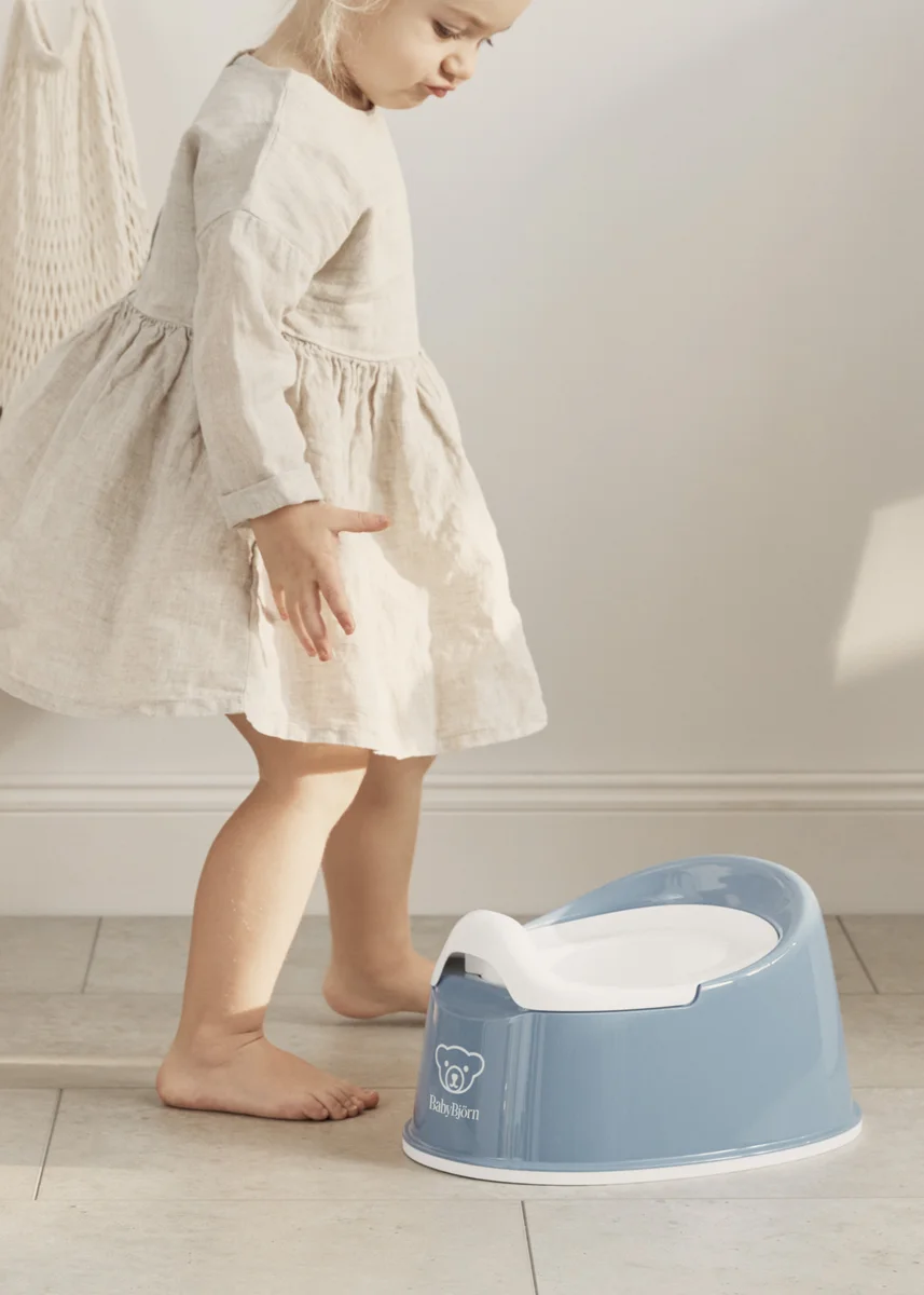 Toddler approaching BabyBjorn Smart Potty on bathroom floor, showing compact low-profile design