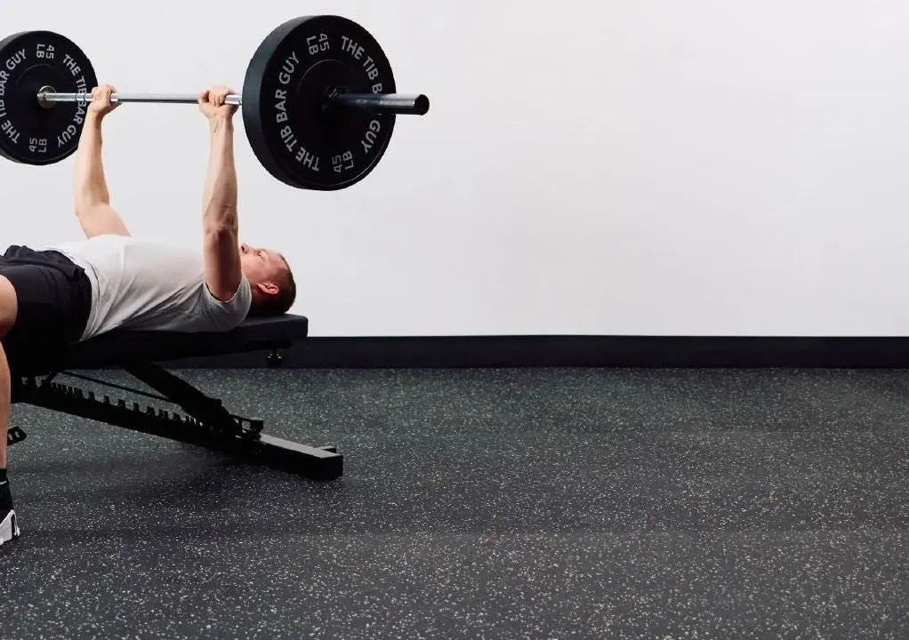 Man performing a barbell bench press on the APEX Adjustable Bench in a home gym