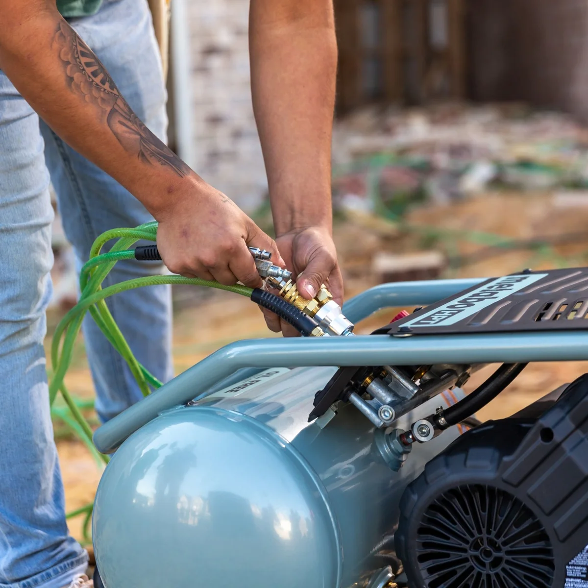 Worker connecting an air hose to the Metabo HPT EC1315SM compressor outlet on a construction site