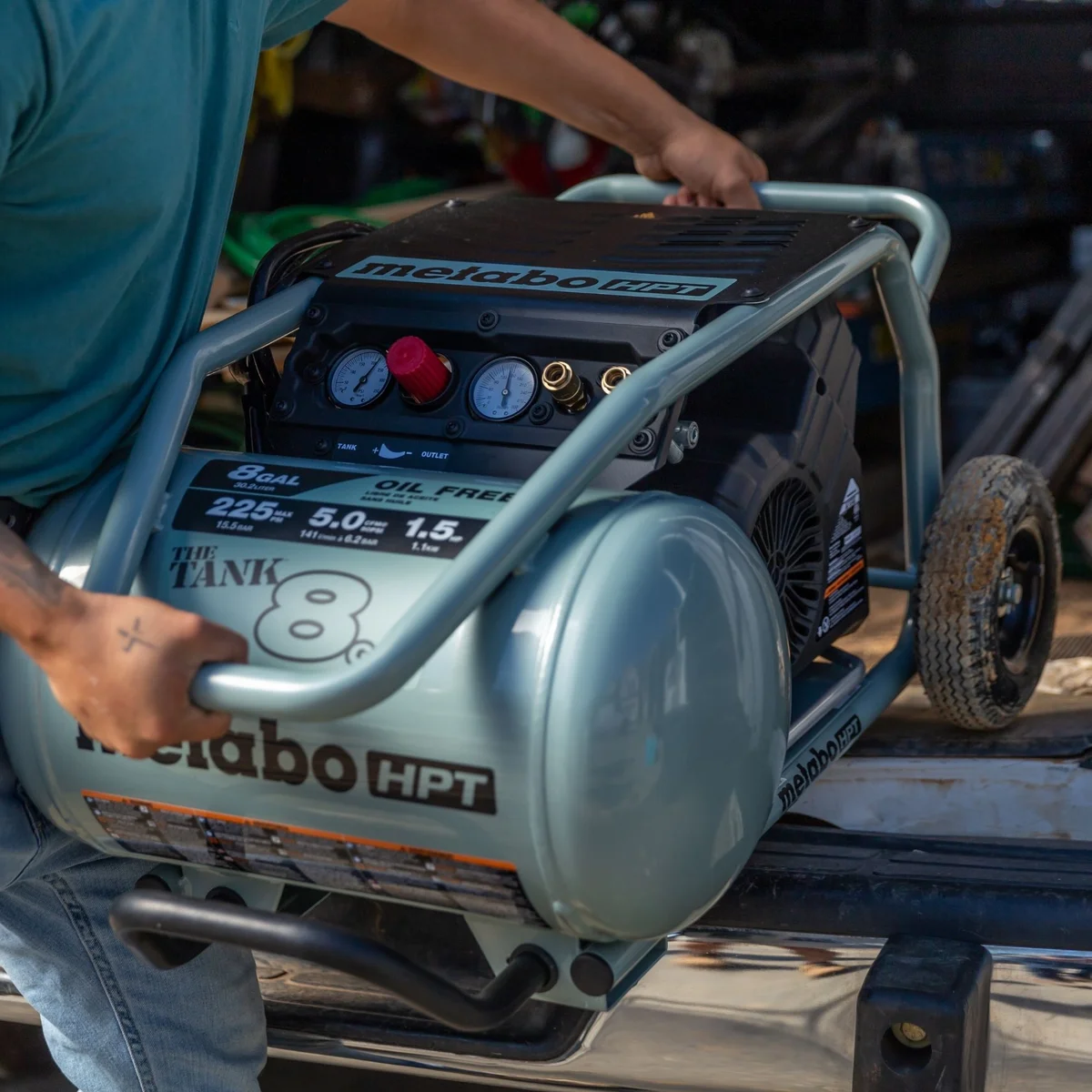 Worker lifting the Metabo HPT EC1315SM air compressor onto a truck bed, showing portability