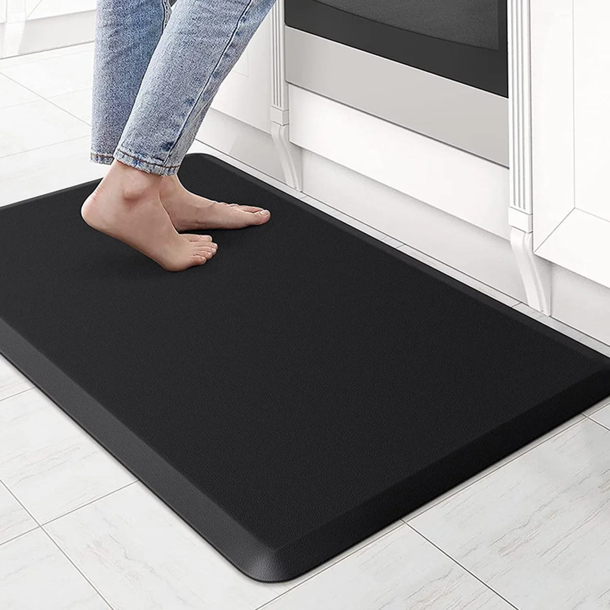 ComfiLife Anti-Fatigue Floor Mat in black, person standing barefoot on it in a kitchen showing the beveled edge