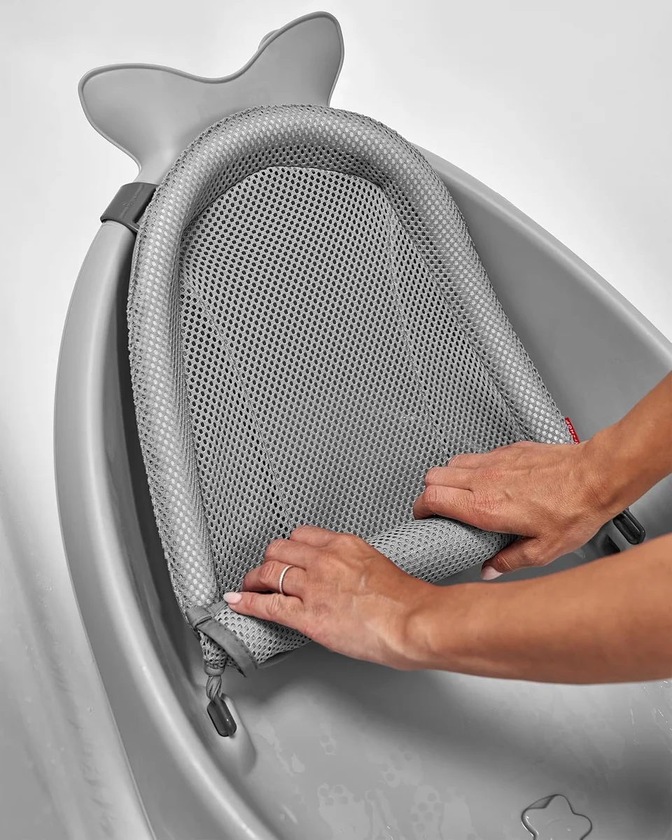 Close-up of hands adjusting the removable grey mesh newborn sling inside the Skip Hop Moby tub