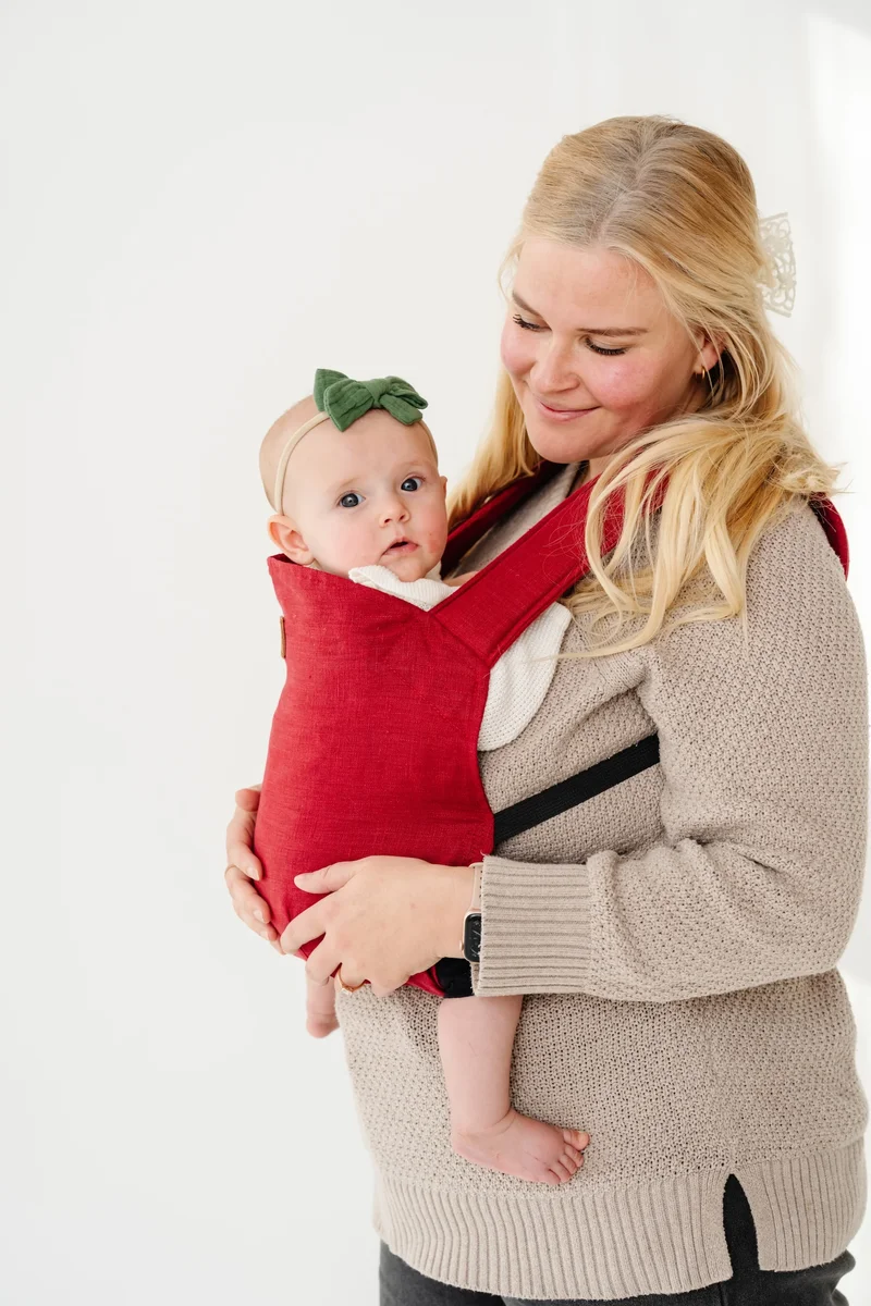 Happy Baby Original carrier in cranberry with an infant in front carry, showing the carrier's structured panel and seat