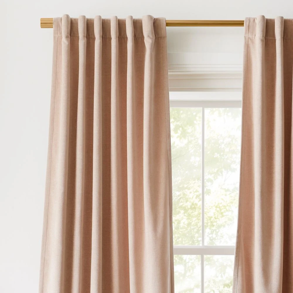 West Elm Worn Velvet Blackout Curtain in blush hung on a brass rod against a bright white wall