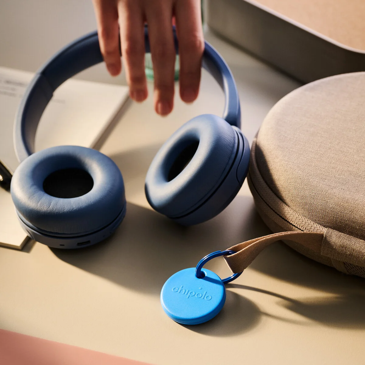 Close-up of the Chipolo POP blue tracker with its keyring carabiner, resting on a desk next to headphones