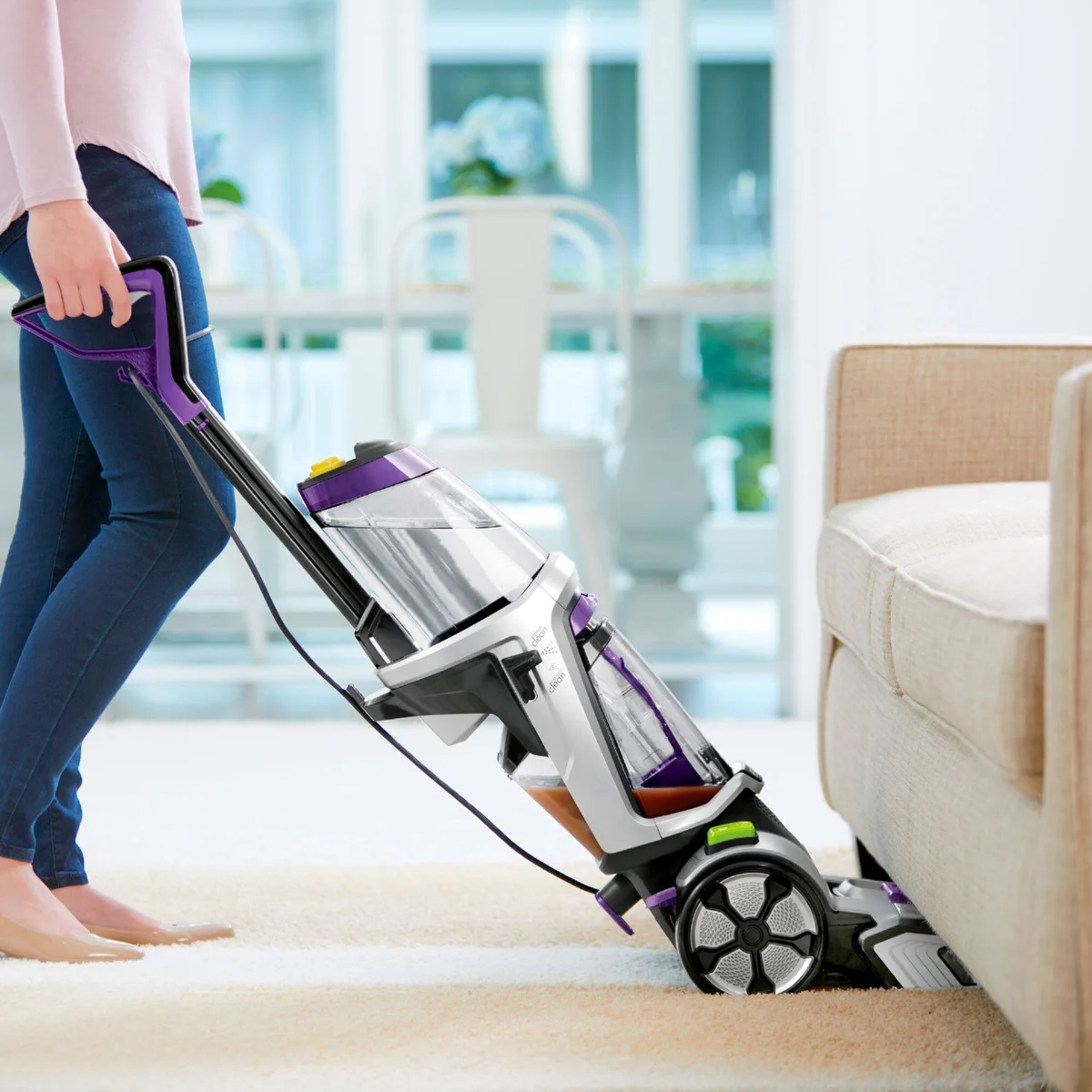 Bissell ProHeat 2X Revolution Pet Pro Plus being pulled back near a sofa, showing side profile and rear wheels