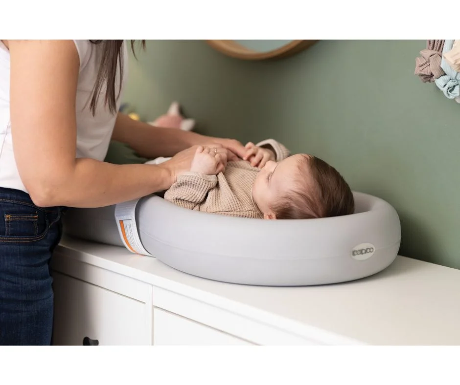 Keekaroo Peanut Changer in grey, in use on a changing table with a newborn, shown in a nursery setting