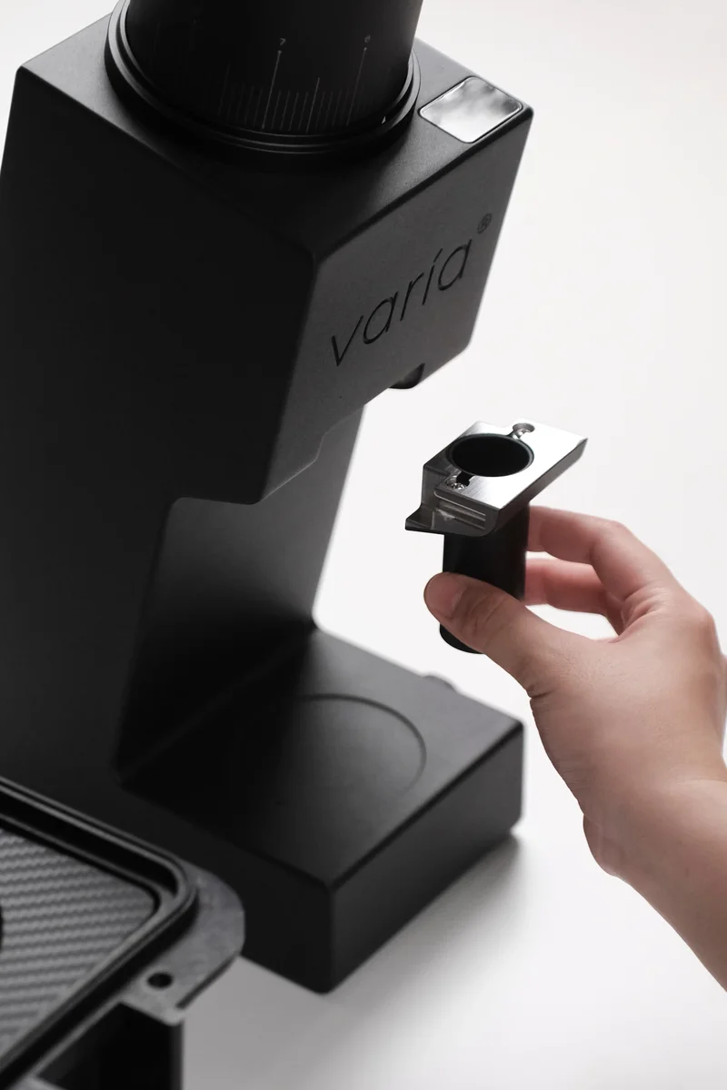 Close-up of the Varia VS6 modular output chute adapter being removed, highlighting the grinder's swappable burr system