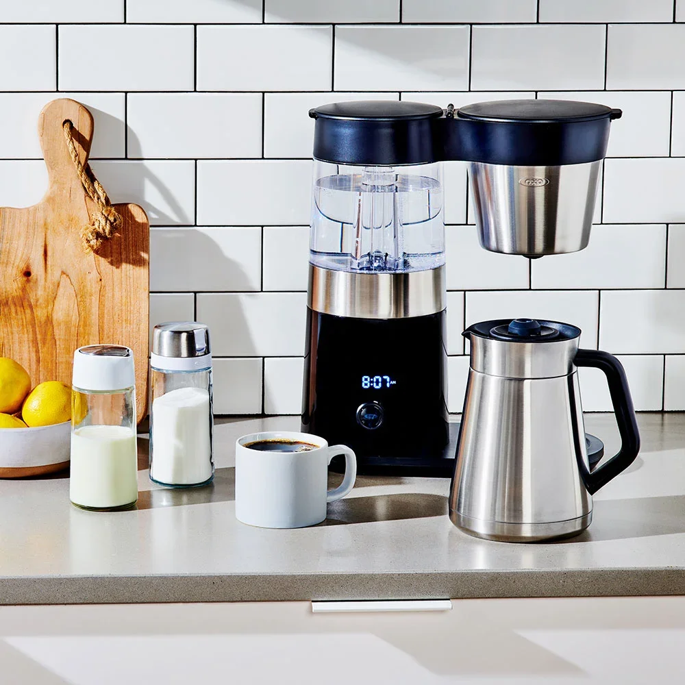 OXO Brew 9-Cup Coffee Maker on a kitchen counter with its stainless thermal carafe beside a cup of coffee