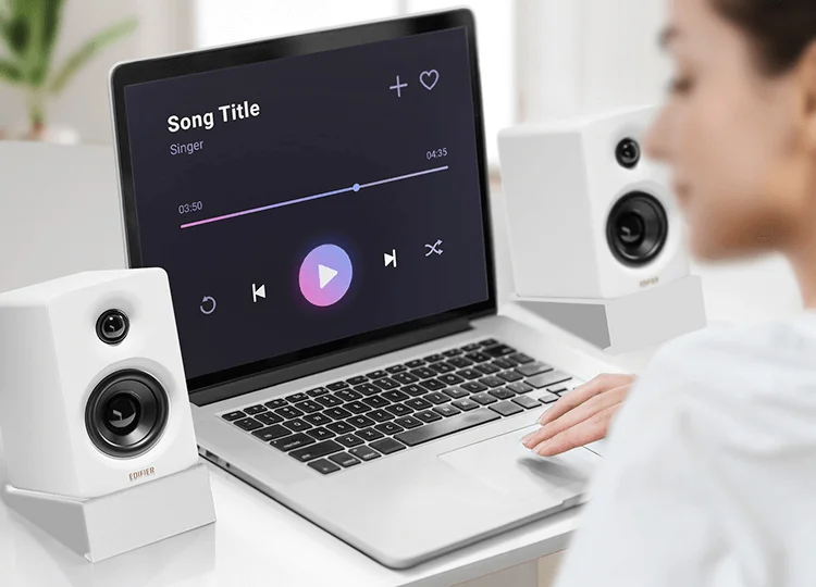 Edifier M60 in white on a desk flanking a laptop with music player, showing compact footprint in a real workspace