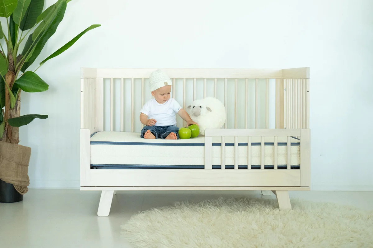 Baby sitting on My Green Mattress Emily in a toddler rail crib