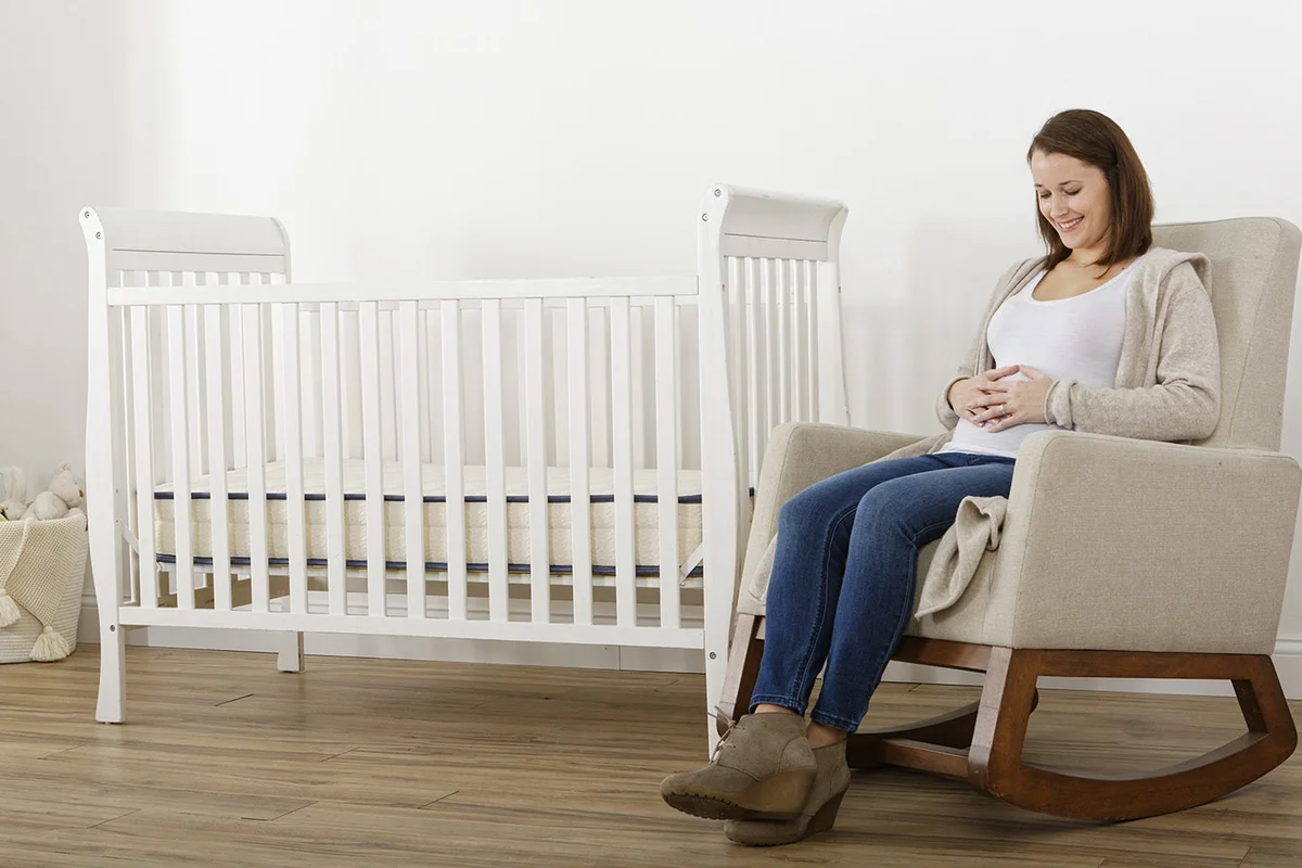 Expectant mother seated beside crib with My Green Mattress Emily in a bright nursery