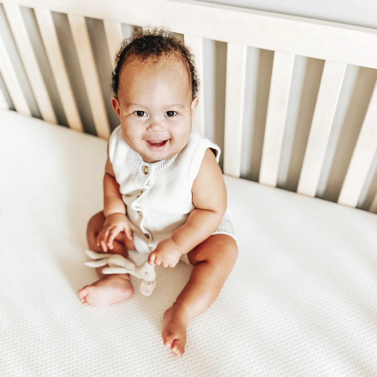 Baby sitting upright on Newton Baby Essential Crib Mattress in white crib