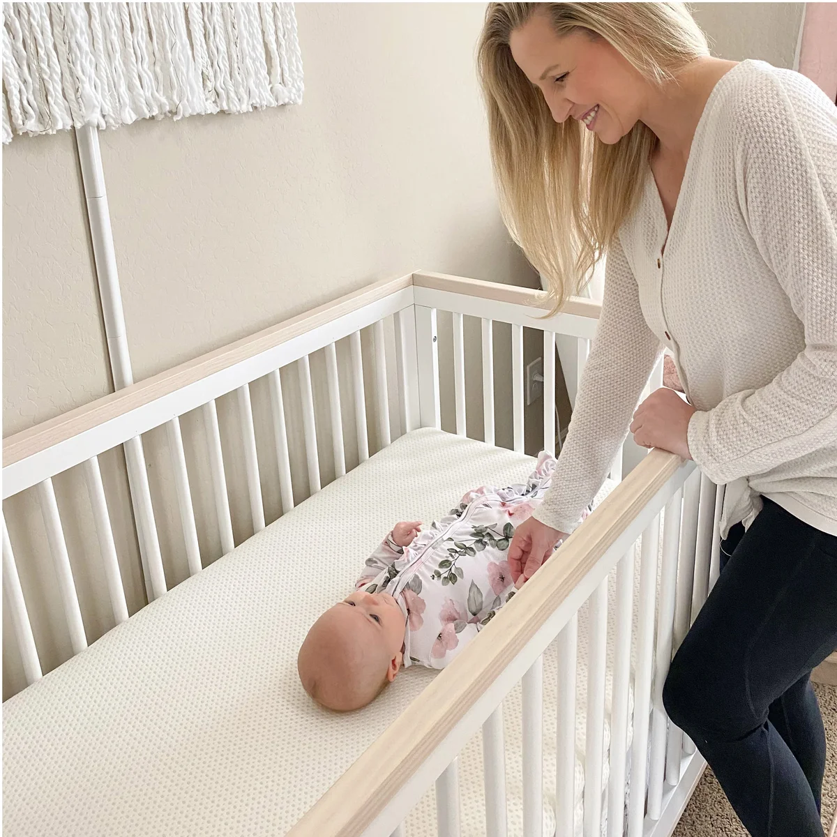 Parent watching newborn sleeping on Newton Baby Essential Crib Mattress in white nursery crib