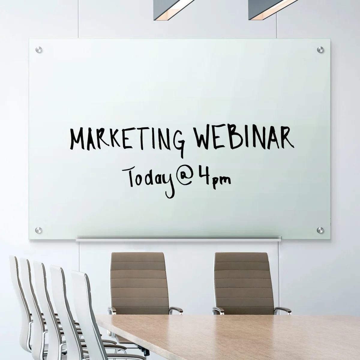 Quartet Infinity glass whiteboard mounted on an office wall above a conference table with handwriting reading Marketing Webinar
