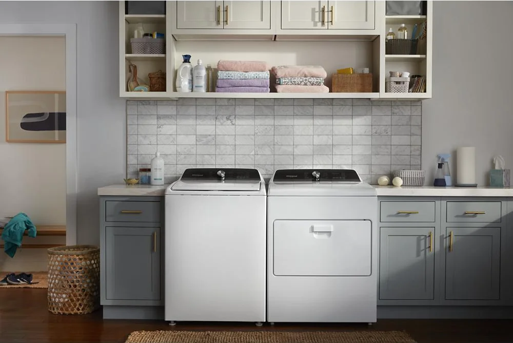 Whirlpool WED5010LW dryer and washer pair in a bright laundry room with gray cabinets and open shelving