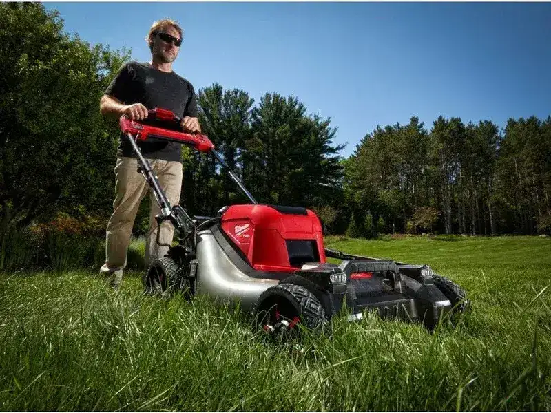 Man pushing the Milwaukee M18 Fuel mower through lush green grass in an open yard