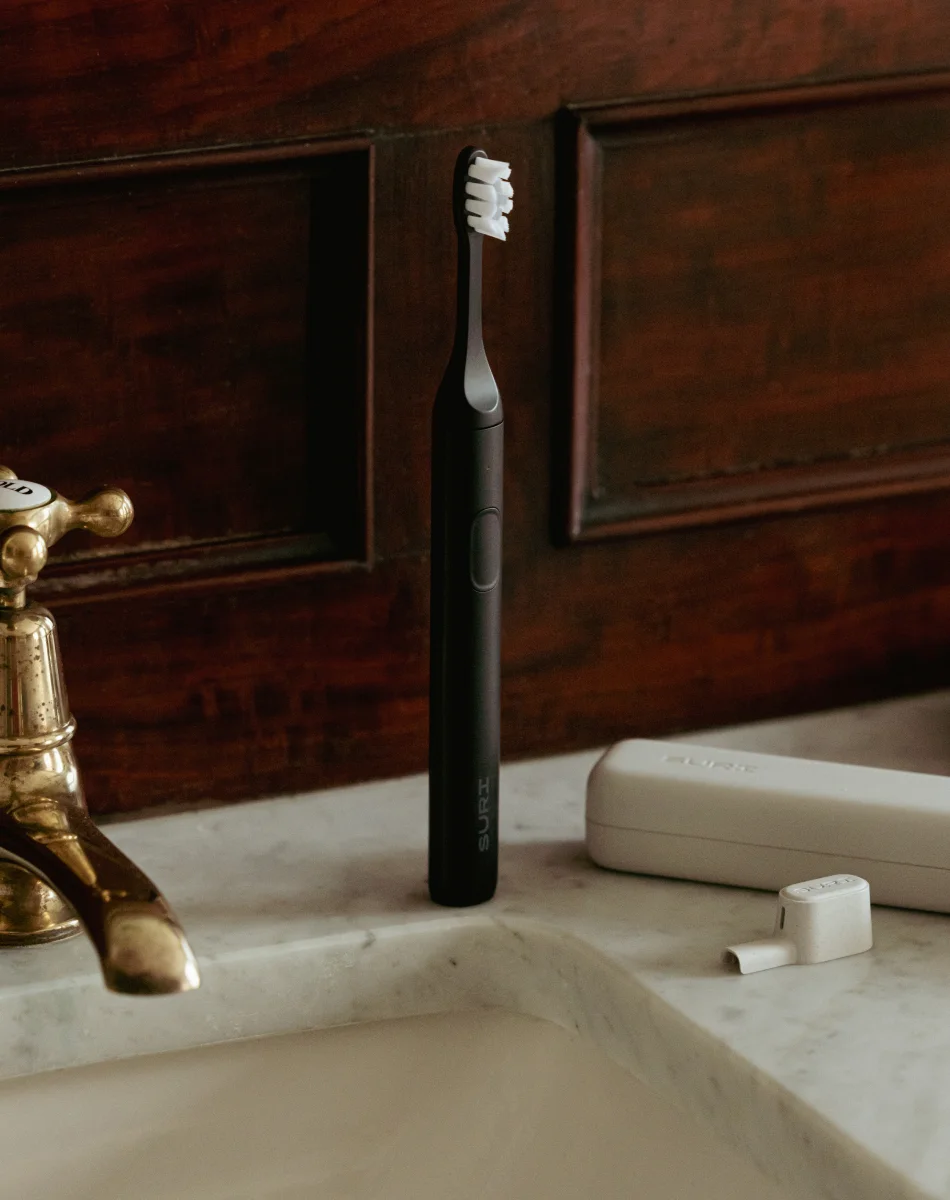 SURI 2.0 toothbrush standing on marble bathroom countertop beside vintage brass tap