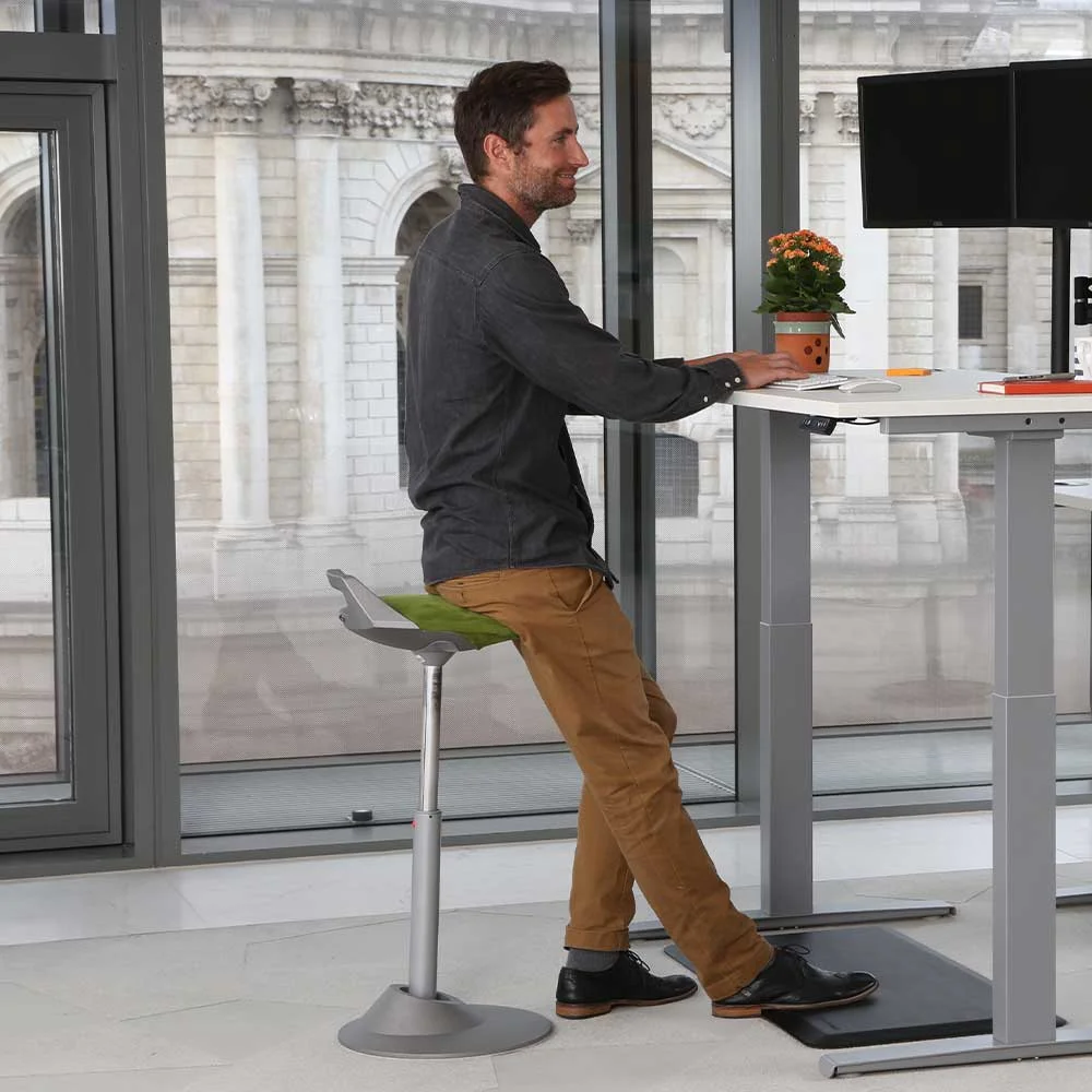 Man leaning on green Aeris Muvman stool at standing desk in modern office