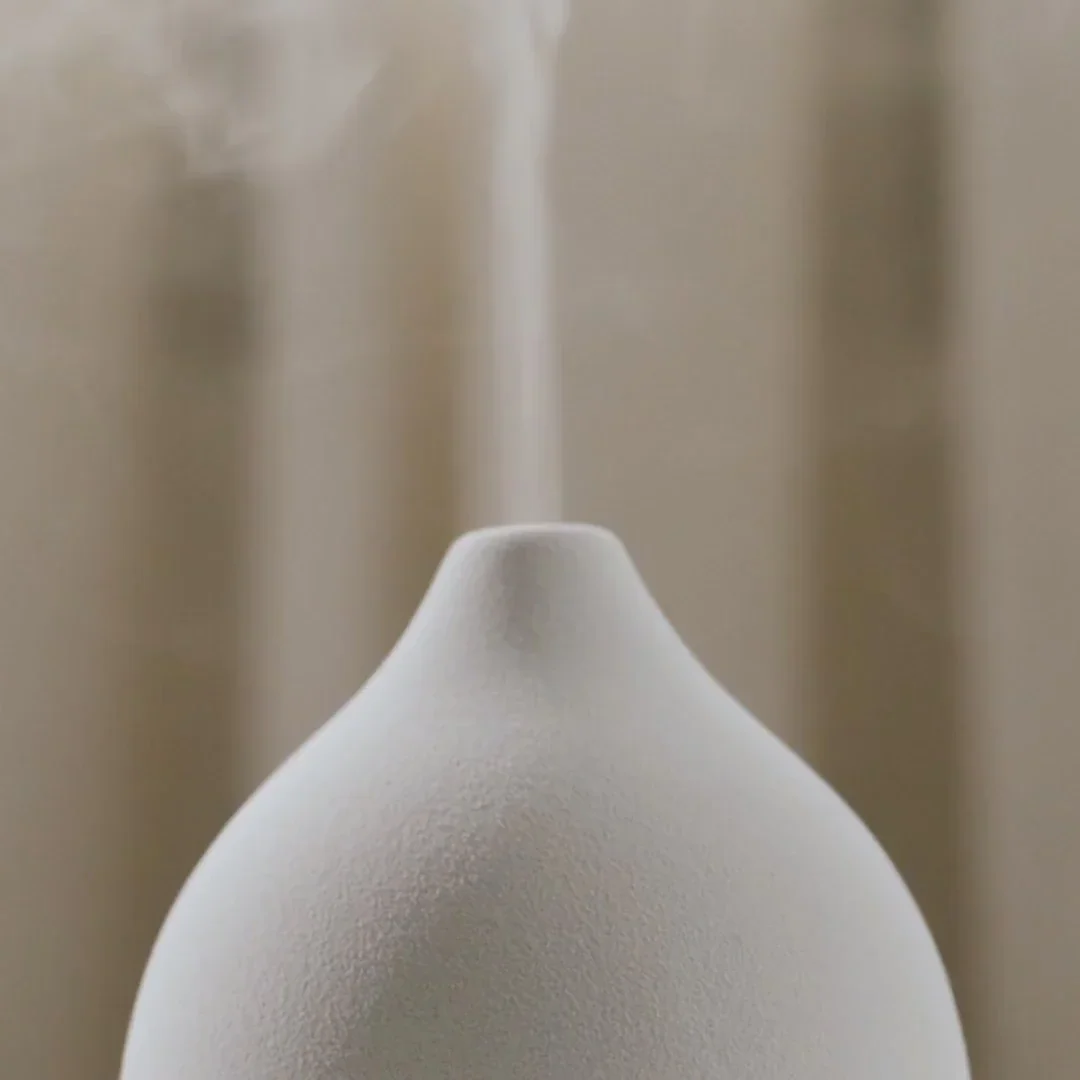 Close-up of the white Vitruvi Stone Diffuser's textured matte ceramic top, with a thin stream of mist rising from the spout
