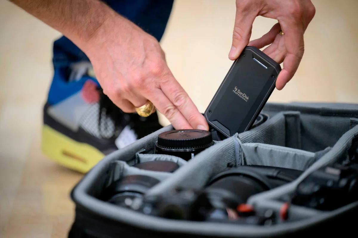 SanDisk Professional PRO-G40 SSD being packed into a camera bag alongside lenses, showing its compact puck shape