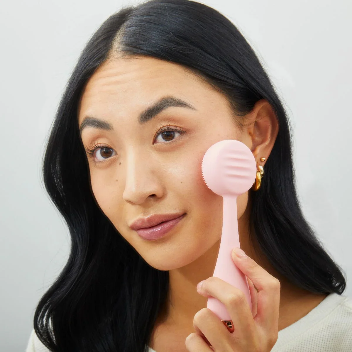 Model holding PMD Clean blush silicone cleansing device against her cheek