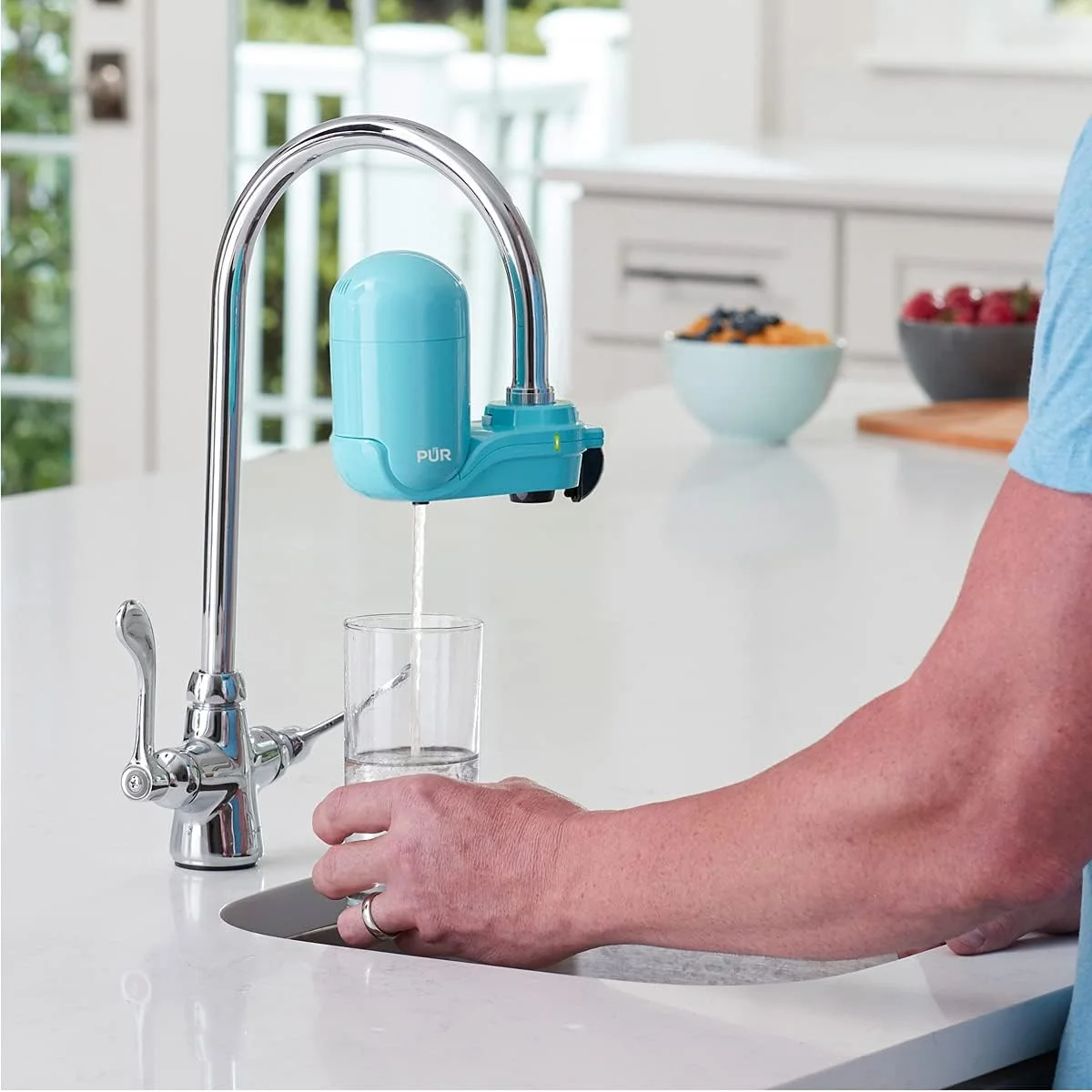 Person filling glass of water using PUR Plus faucet filter