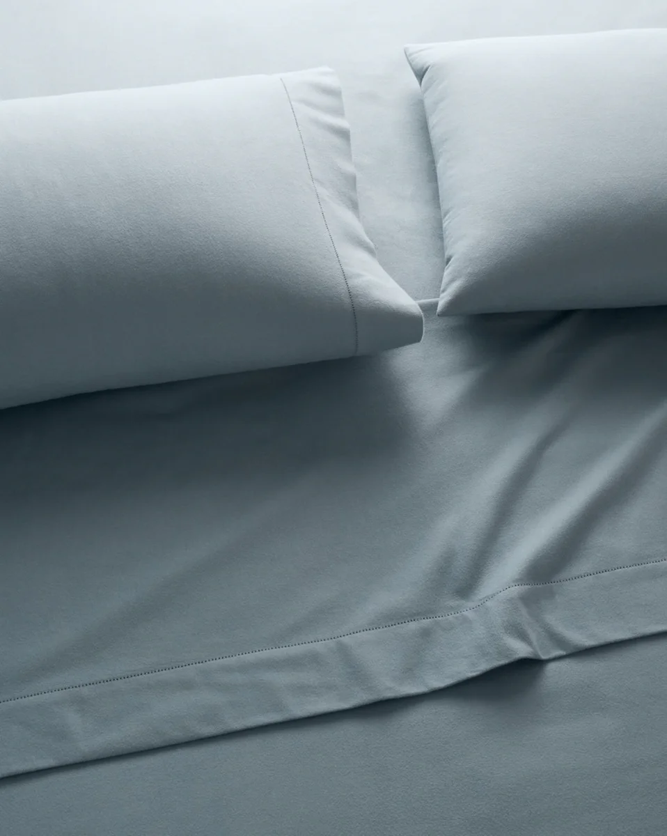Garnet Hill Solid Hemstitched Pima Cotton Flannel Sheets in blue-grey, made bed with pillows showing hemstitch hem detail
