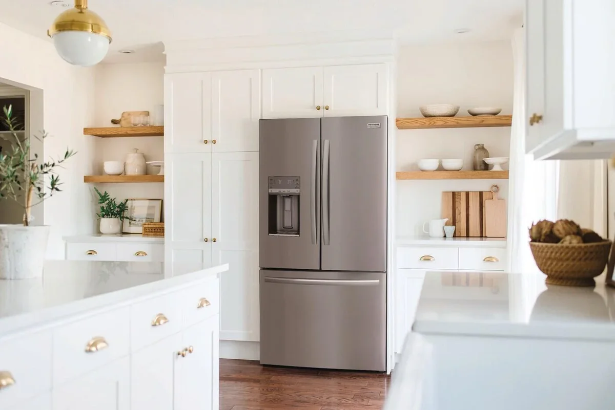 Frigidaire Gallery GRFS2853AF installed in a white kitchen with wood open shelving and gold hardware