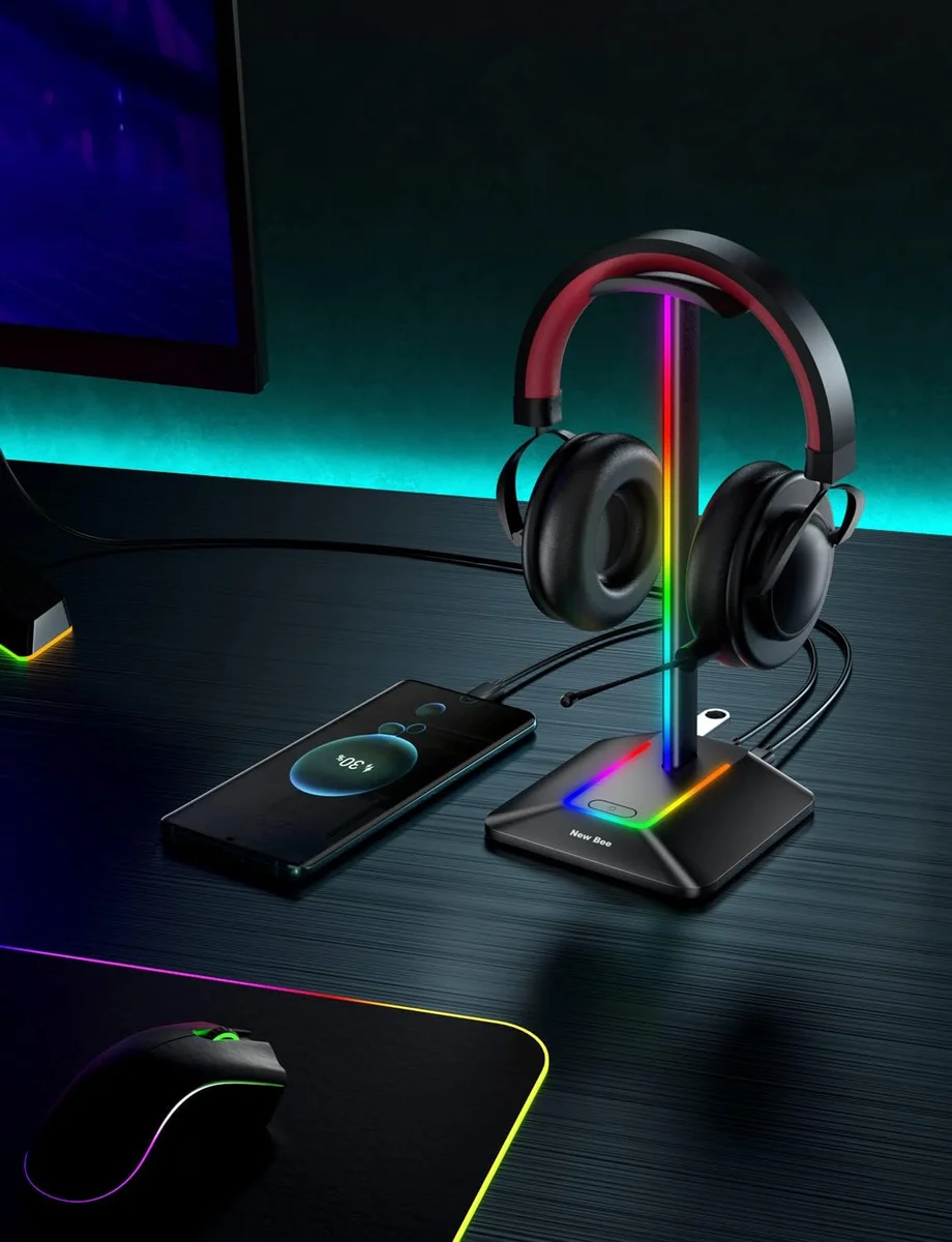 New Bee RGB headphone stand on a gaming desk with a headset resting on it and a phone charging beside an RGB mousepad