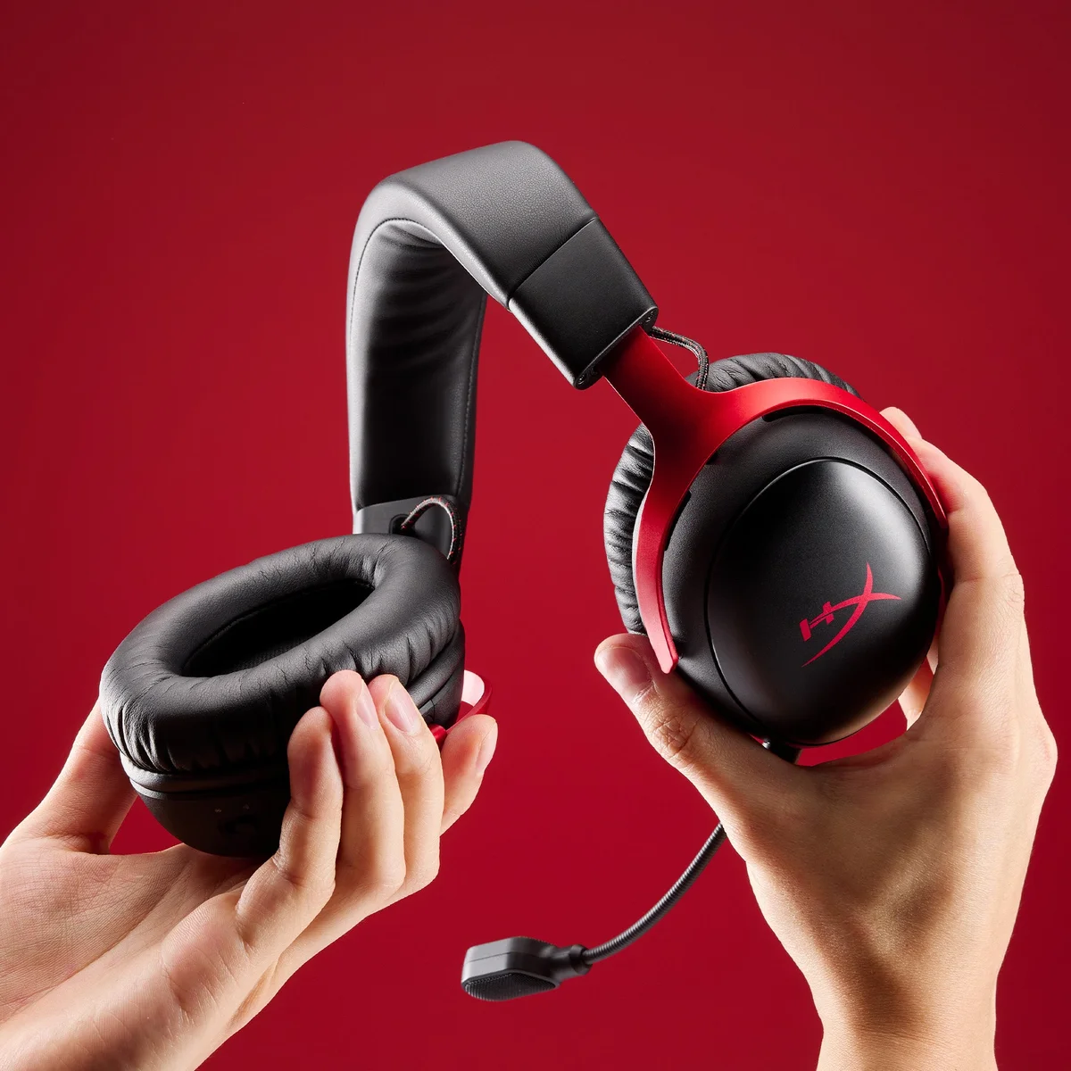 Hands holding the HyperX Cloud III S Wireless in black and red, showing plush leatherette ear cushions and build quality