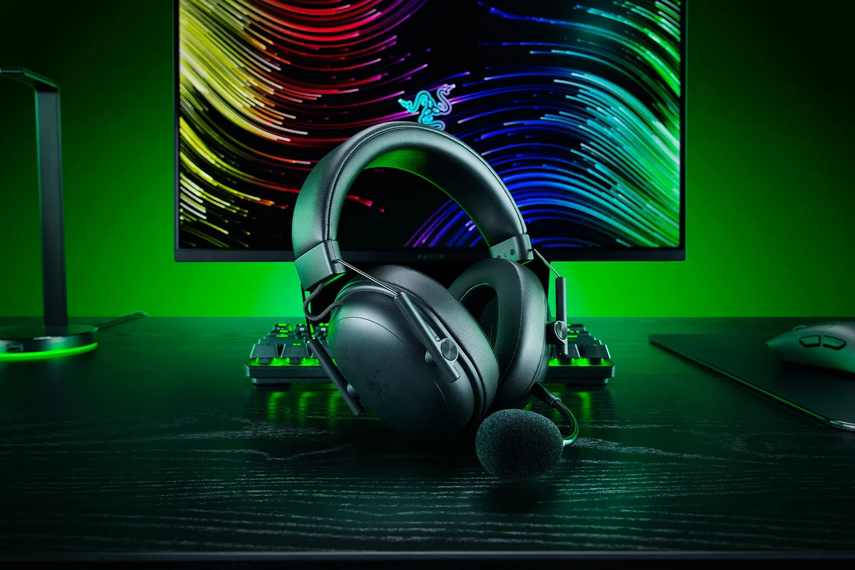 Razer BlackShark V3 X HyperSpeed standing on a gaming desk in front of a monitor and keyboard with green ambient lighting