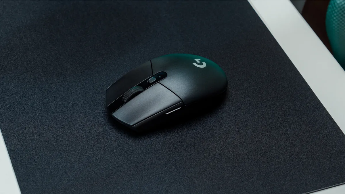 Black Logitech G305 Lightspeed resting on a dark cloth mousepad at a desk