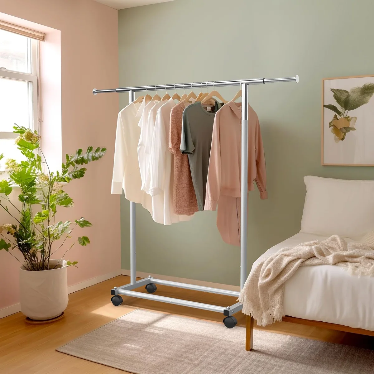 Simple Houseware Standard Rod Garment Rack loaded with shirts and blouses in a bedroom beside a bed and potted plant