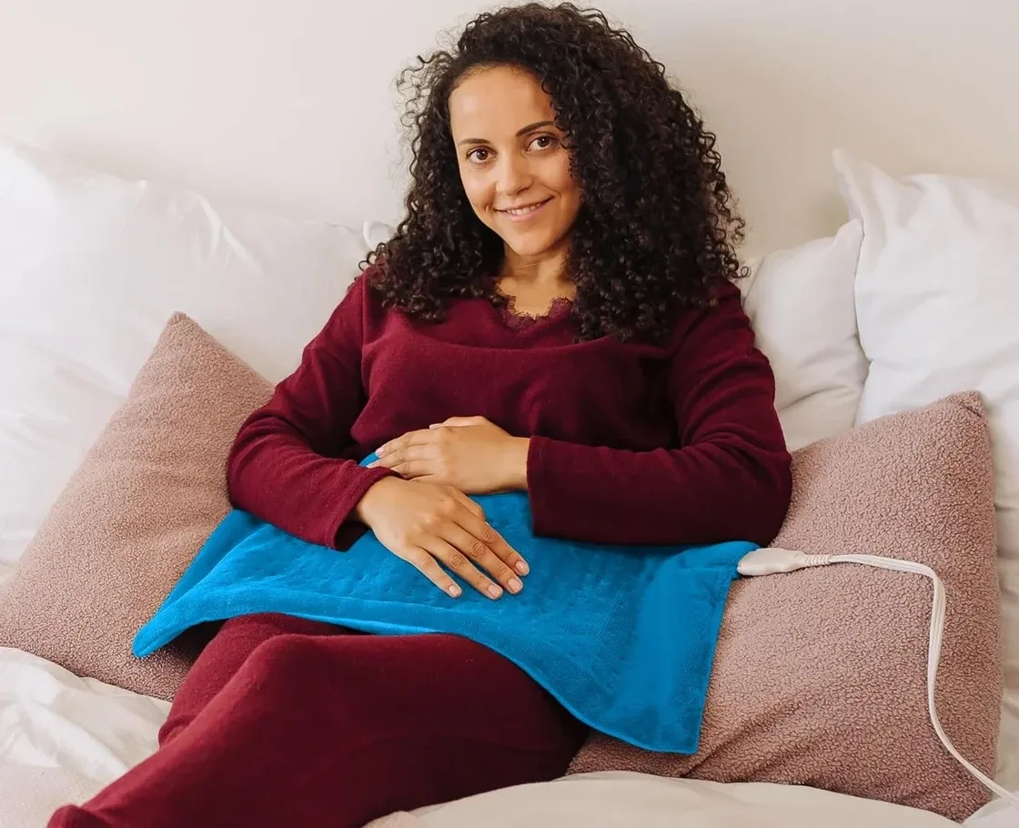 GENIANI heating pad in use on lower abdomen while seated on a bed