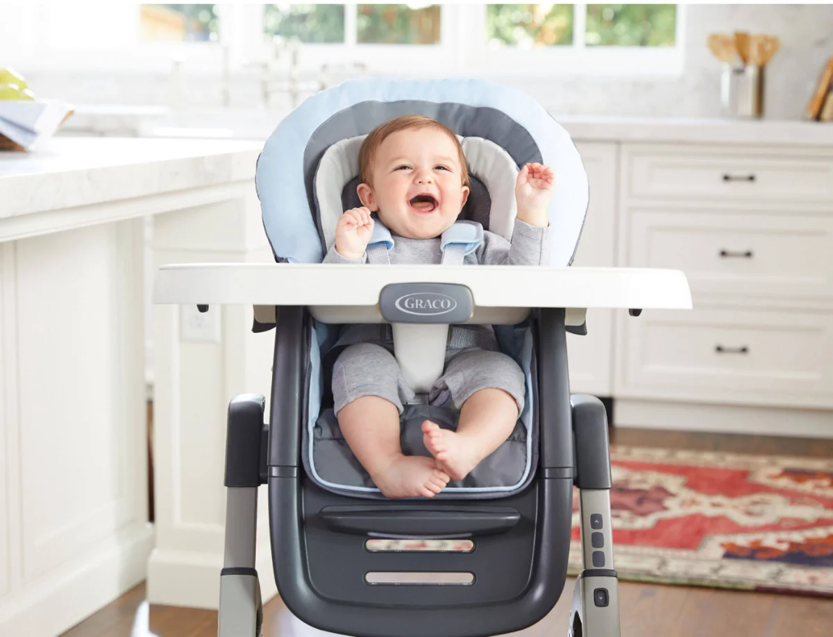 Happy infant secured in Graco DuoDiner DLX seat with padded insert and 5-point harness