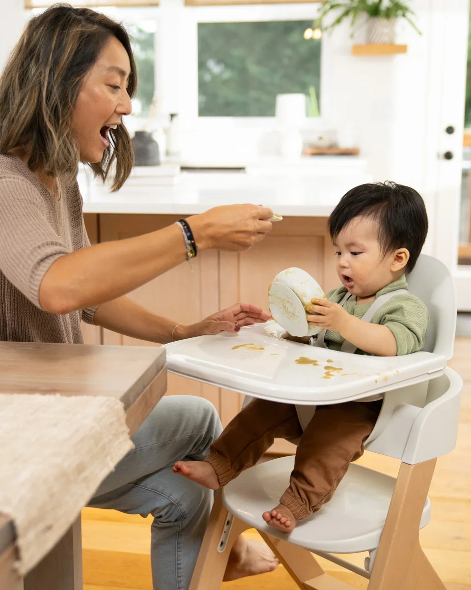 Parent feeding baby in Mockingbird High Chair, showing easy-clean tray during messy mealtime