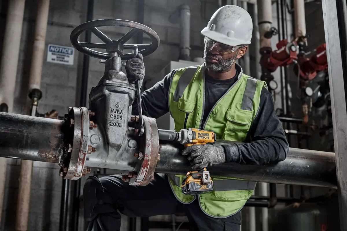 DeWalt DCF891 Mid-Torque Impact Wrench in use by worker tightening industrial pipe flange bolts